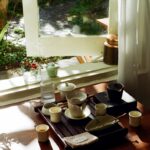 “바쁜 일상 속 작은 변화로 지키는 직장인 건강… 일상 속 실천법 주목” Tea set arranged on a wooden tray by the window.